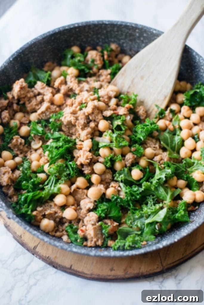 Close-up shot of a skillet filled with uncooked Italian chicken sausage, chickpeas, and fresh kale, demonstrating the simple, wholesome ingredients before cooking.
