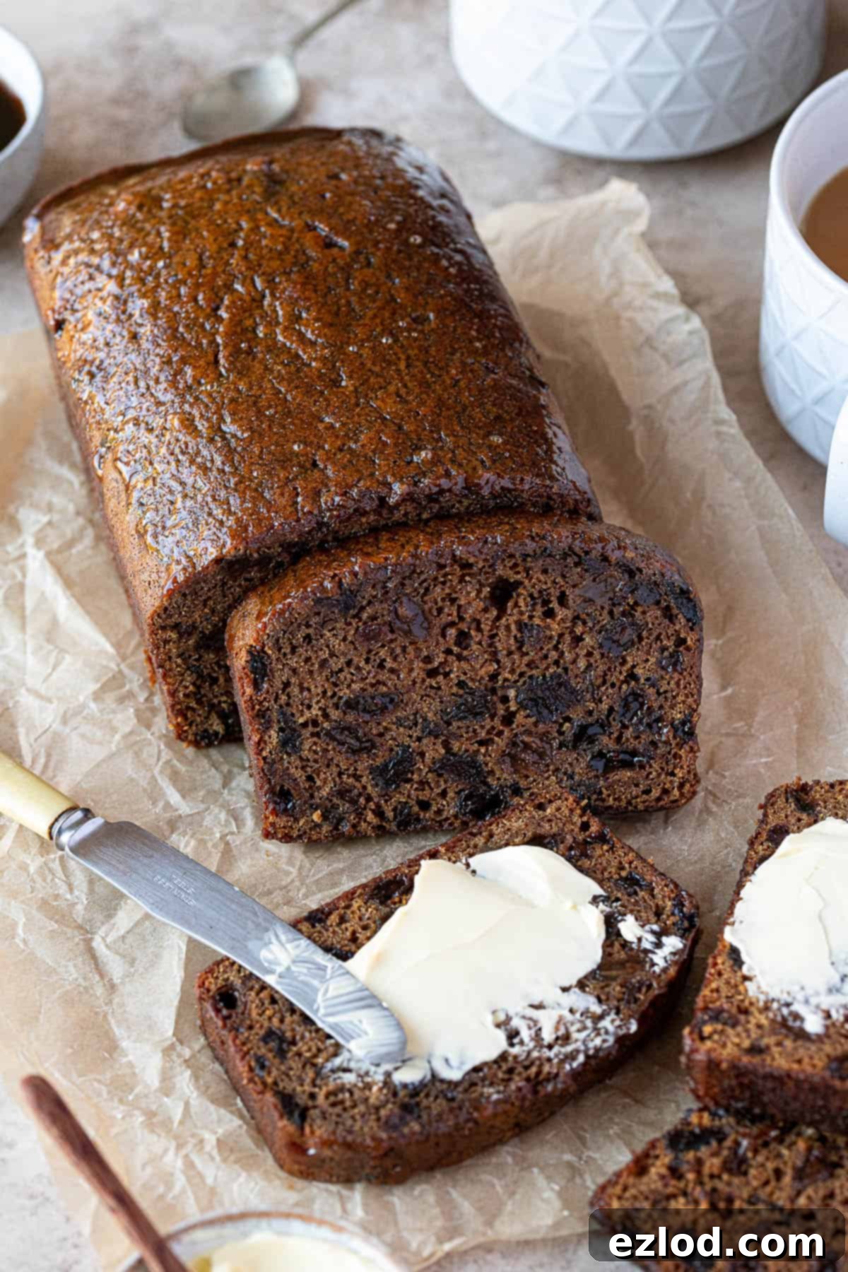 Sliced vegan malt loaf on a sheet of baking parchment, a couple of slices spread with butter.