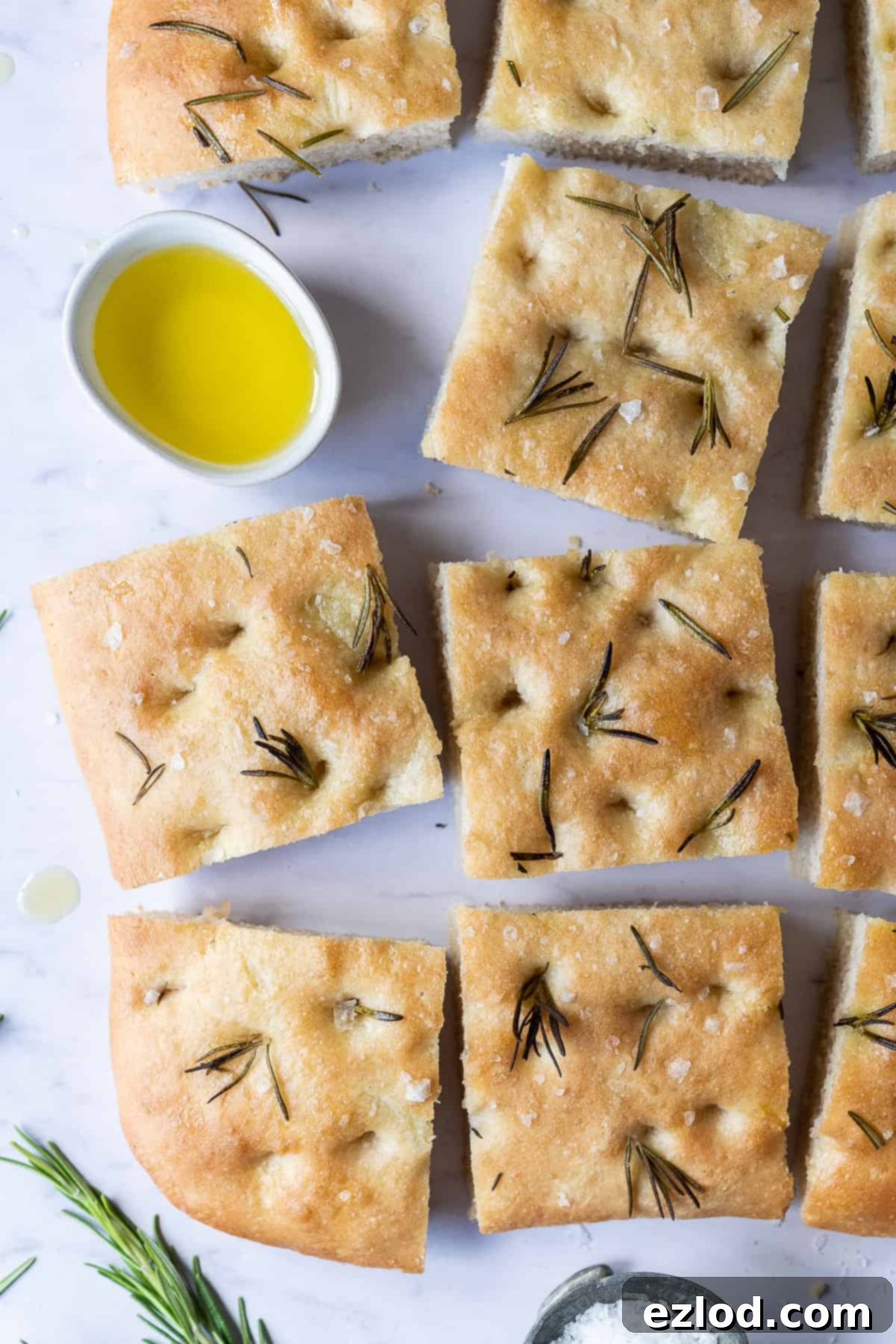 Perfectly cut squares of golden sea salt and rosemary focaccia arranged around a small bowl of olive oil for dipping.
