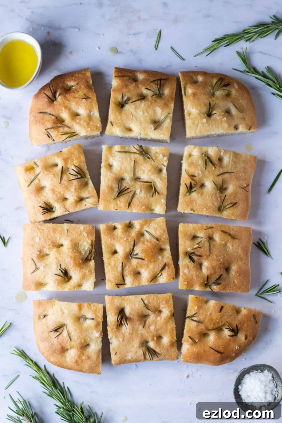 Delicious squares of freshly baked focaccia with sea salt and rosemary, arranged on a elegant marble background.