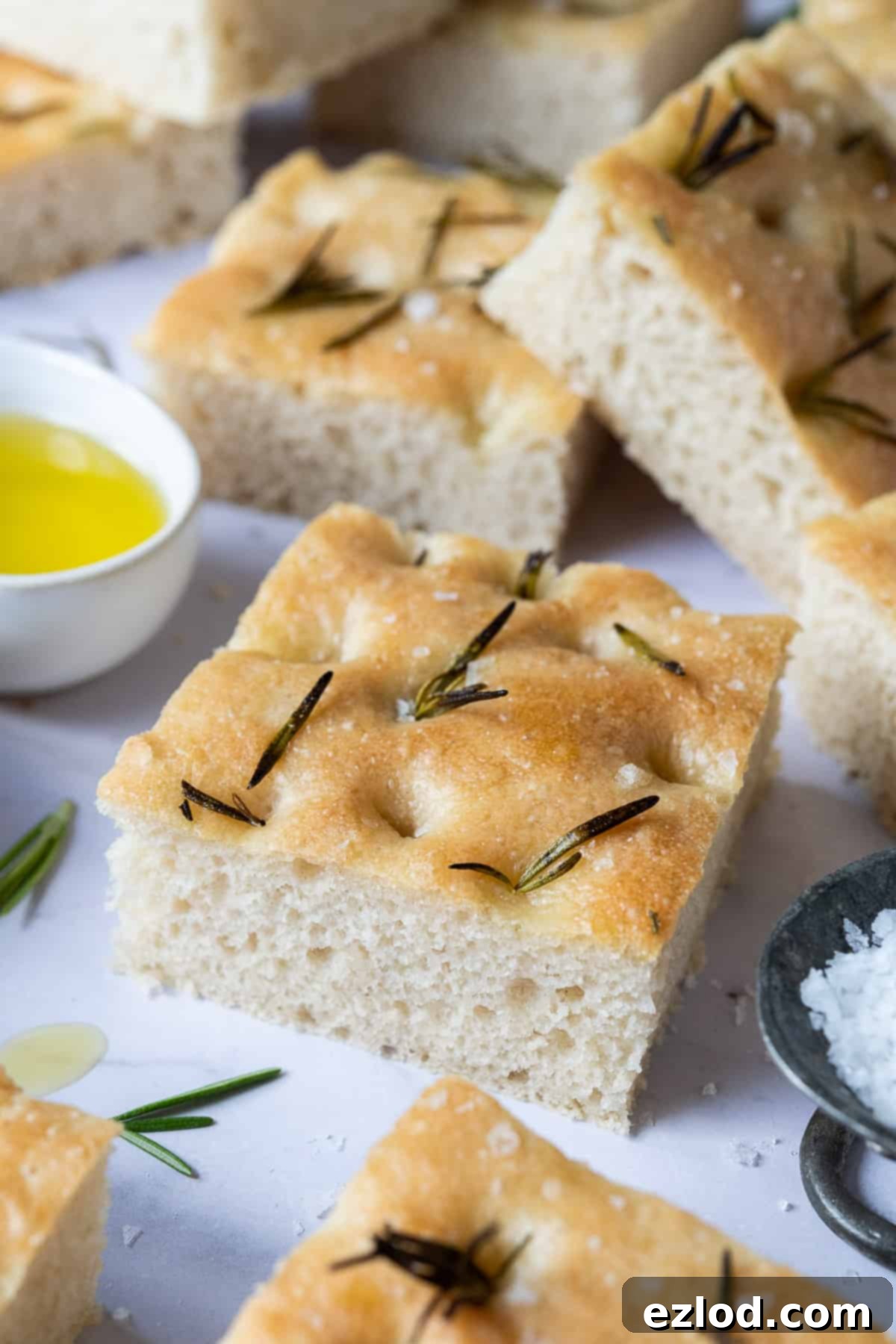 Close-up detail of a single square of golden focaccia, highlighting its dimpled surface, fluffy interior, and rosemary sprigs.