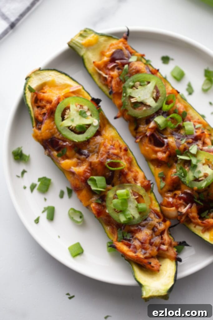 Overhead image: zucchini sliced lengthwise and stuffed with BBQ chicken and topped with cheese, all cooked and on a white plate