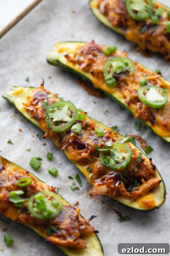 Overhead image: halved bbq chicken stuffed zucchinis on a parchment lined sheet pan