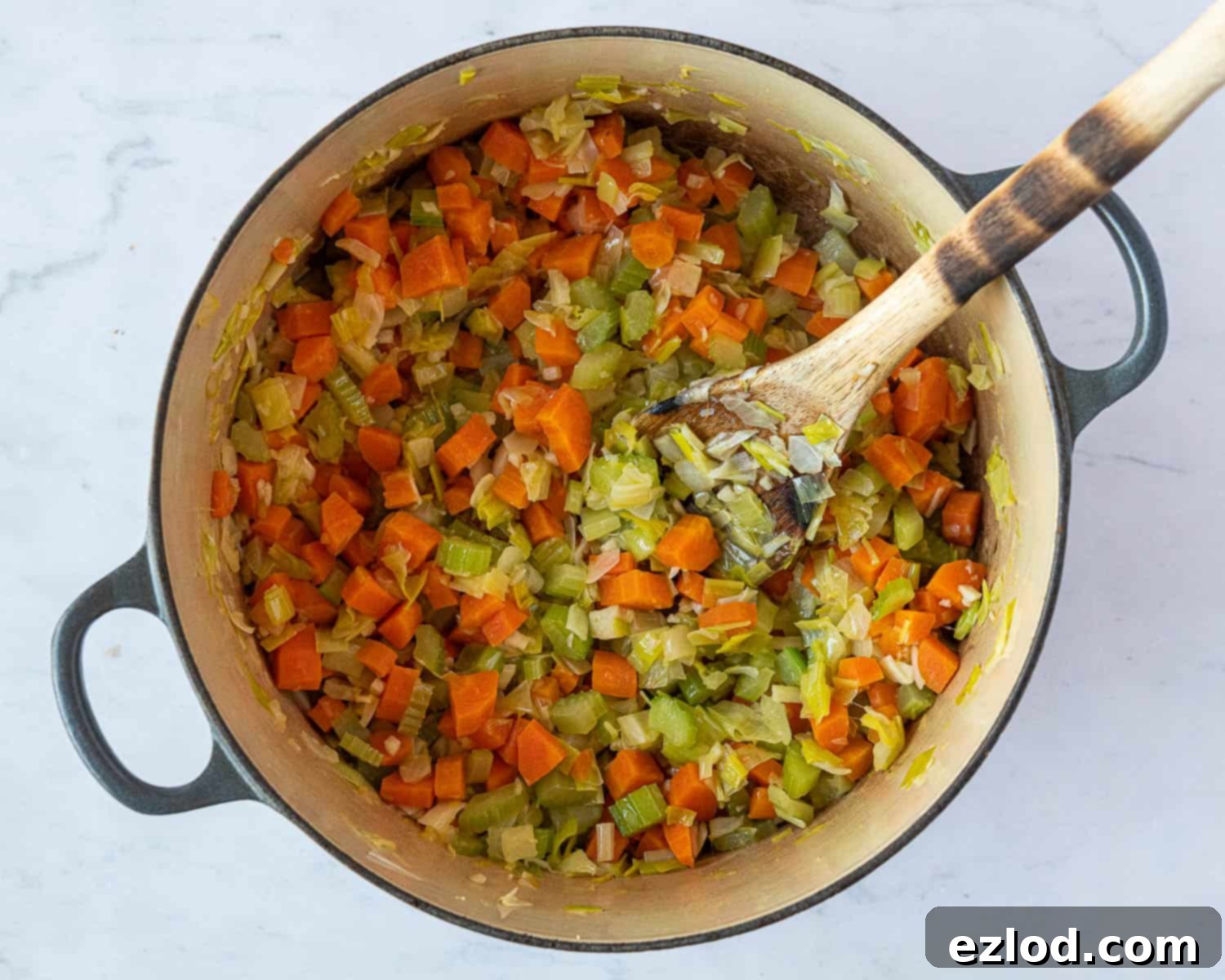 Close-up view of diced onions, leeks, celery, carrots, and garlic sautéing in a pan with vegan butter and olive oil.