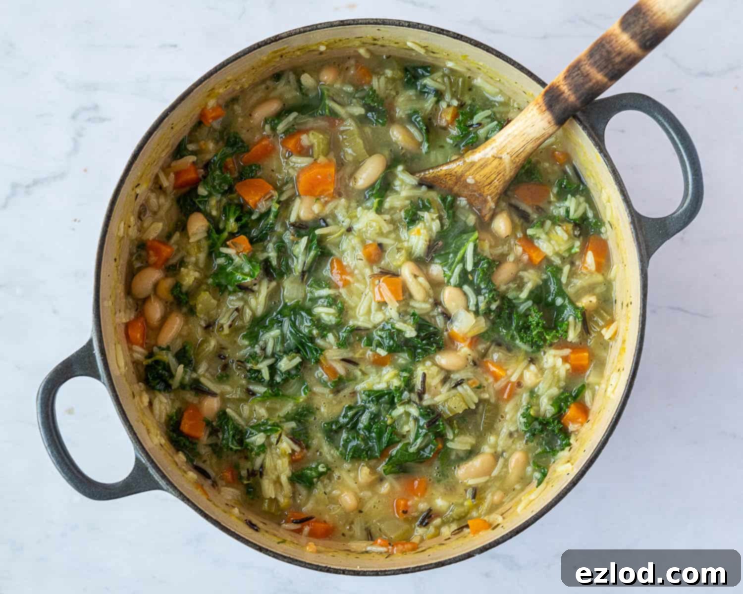Fresh shredded kale being added to the simmering creamy vegetable rice soup in a large pot.