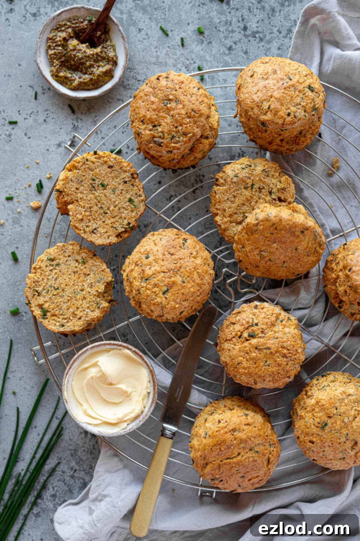Savoury vegan scones on a wire cooling rack with bowls of butter and mustard and fresh chives. A perfect plant-based snack or light lunch.