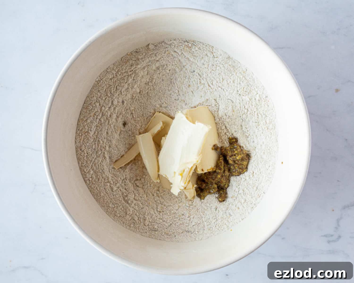 Step 2: Adding cold vegan block butter (cubed) and wholegrain mustard to the bowl of dry ingredients.