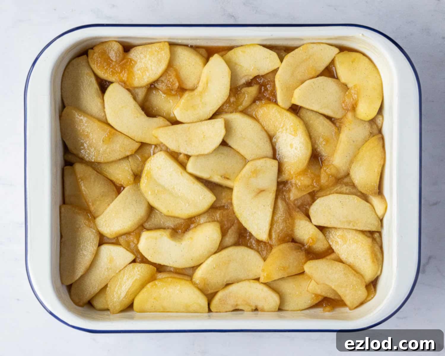 Step 2 in making vegan Eve's pudding: The cooked, slightly softened apples are evenly spread in a greased baking dish, forming the base layer for the sponge topping.