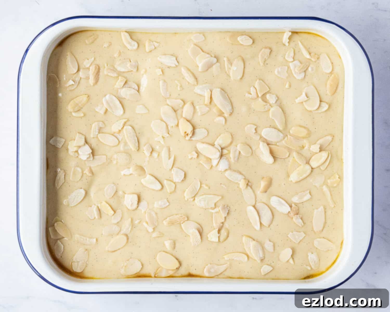Step 4 in making vegan Eve's pudding: The unbaked pudding, with the vegan sponge batter evenly spread over the apple base and topped with a scattering of flaked almonds, ready for the oven.