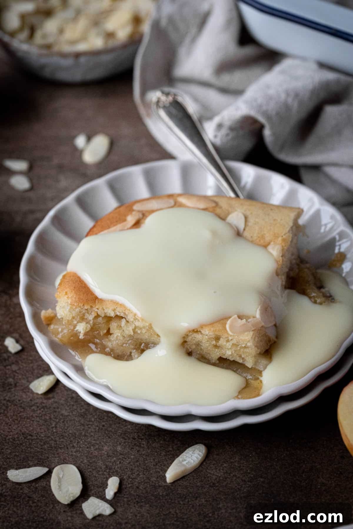 A perfectly portioned slice of vegan Eve's pudding, generously topped with creamy custard, presented on a white plate, ready to be enjoyed.