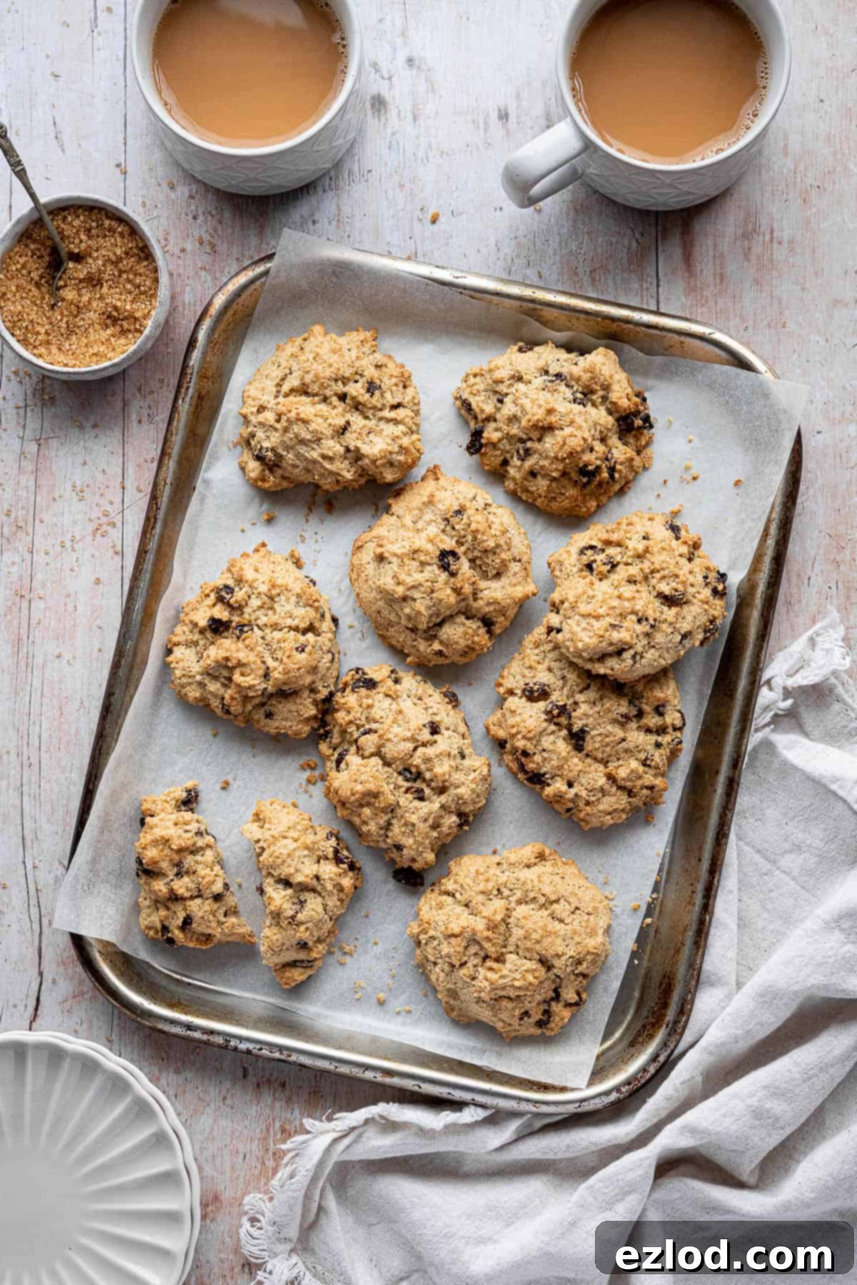 A tray of freshly baked vegan rock cakes served with cups of tea, plates, and a bowl of sugar, evoking a cozy afternoon tea scene.