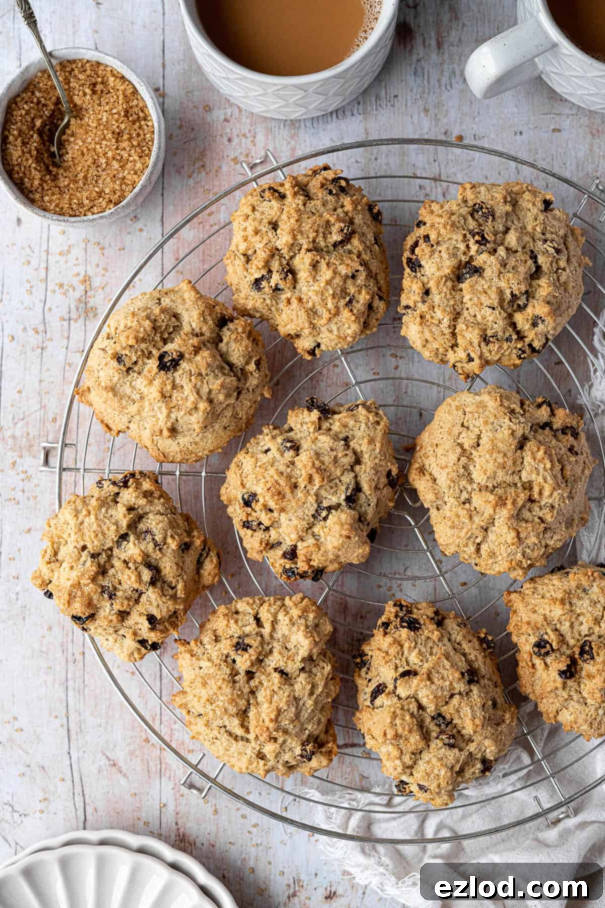 Vegan rock cakes cooling on a round wire rack, accompanied by cups of tea and a bowl of sugar, suggesting a relaxed tea time.
