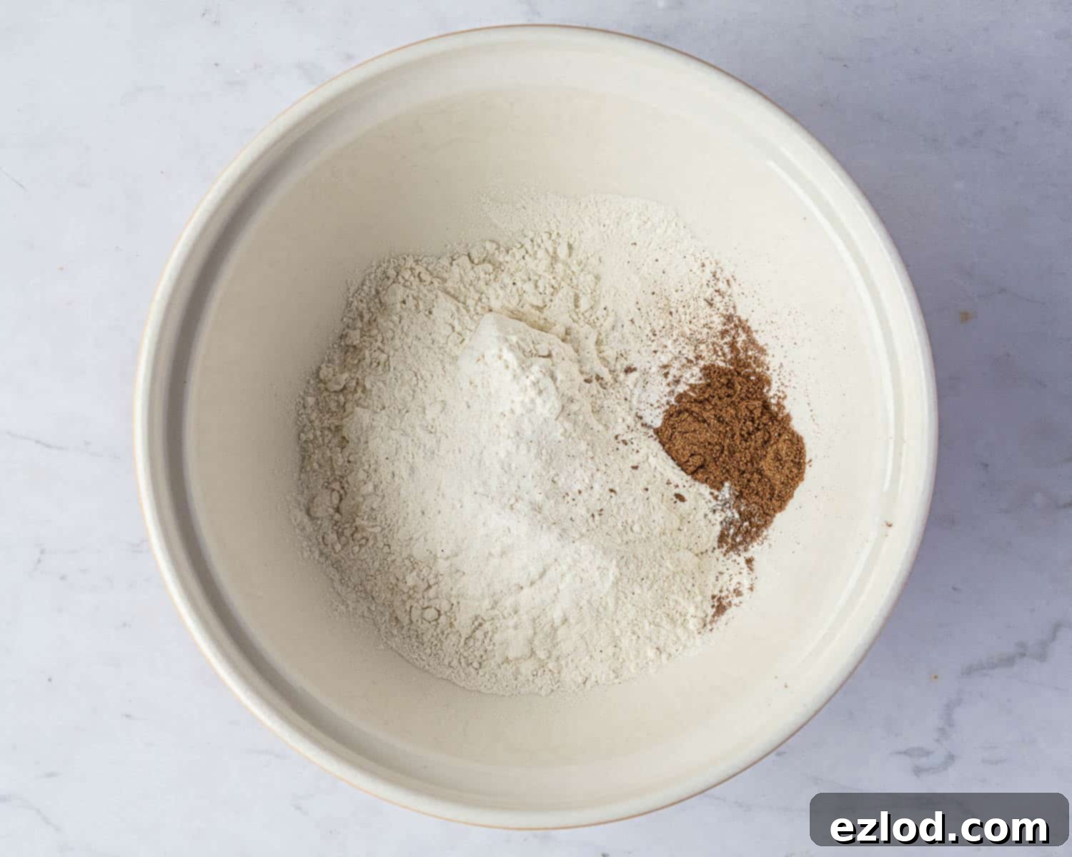 Step 1 in making vegan rock cakes: A bowl containing the dry ingredients – flour, baking powder, and mixed spice – perfectly mixed.
