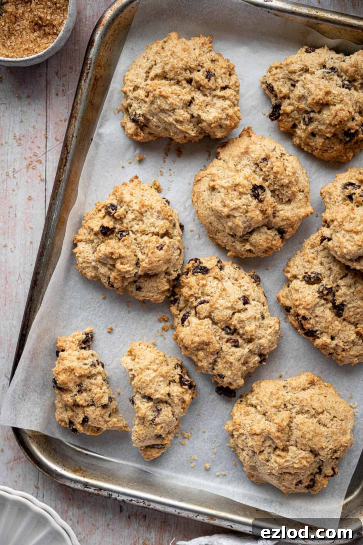 A collection of vegan rock cakes on a metal tray, with one split in half to show its soft interior.