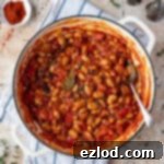 Hearty Smoky Tomato Beans 6 A rustic white pan brimming with rich, smoky tomato beans, garnished with fresh thyme. Surrounding it are a small bowl of vibrant paprika, and salt and pepper shakers.