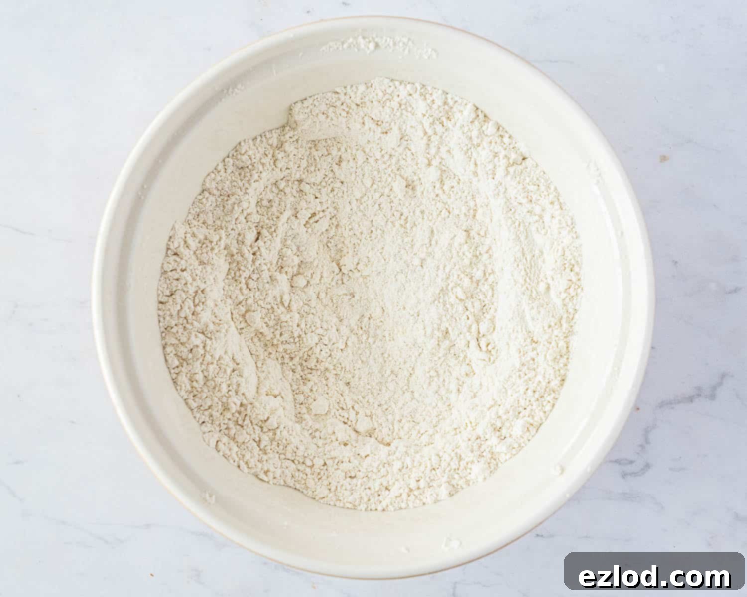 Step 1: A bowl containing the sifted dry ingredients for the vegan chocolate chip vanilla cake recipe.
