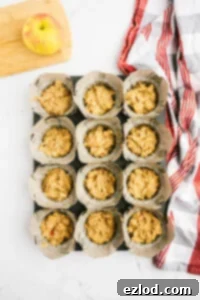 Muffin batter divided into parchment-lined muffin tin, topped with raw sugar.