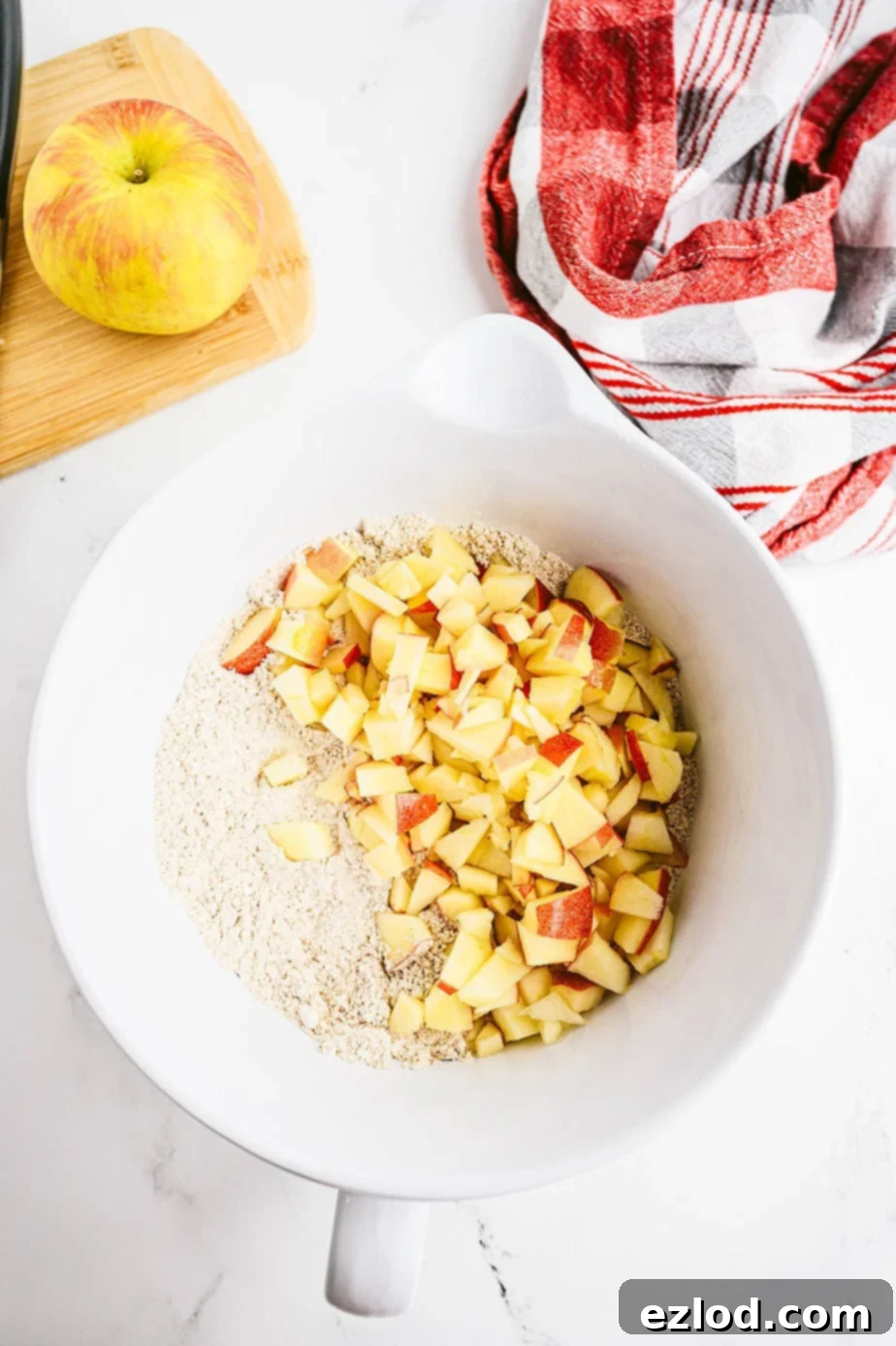 Overhead photo of dry muffin ingredients in a bowl with chopped apples added.