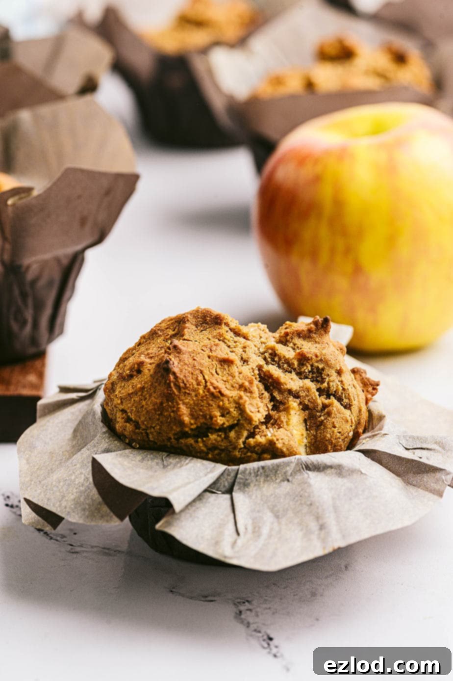 Side view: Healthy apple muffin wrapped in parchment, with many muffins in the background