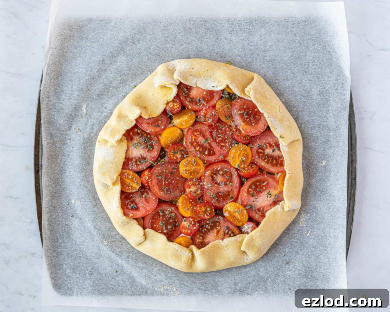 The fully assembled vegan tomato ricotta galette with its rustic folded edges, topped with tomatoes and herbs, ready for baking.