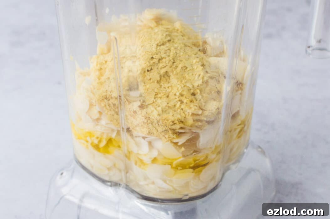 Close-up of the almond cheese ingredients, including soaked flaked almonds, lemon juice, olive oil, garlic, and nutritional yeast, ready to be blended in a food processor.