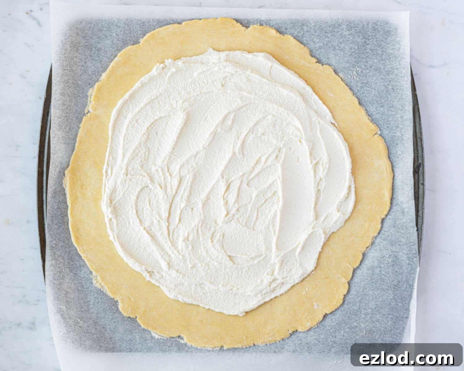 The rolled-out pastry crust, generously spread with the creamy almond cheese, leaving a border for folding.
