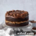 Vegan German chocolate cake on a glass cake stand with bowls of pecans, coconut and ganache.