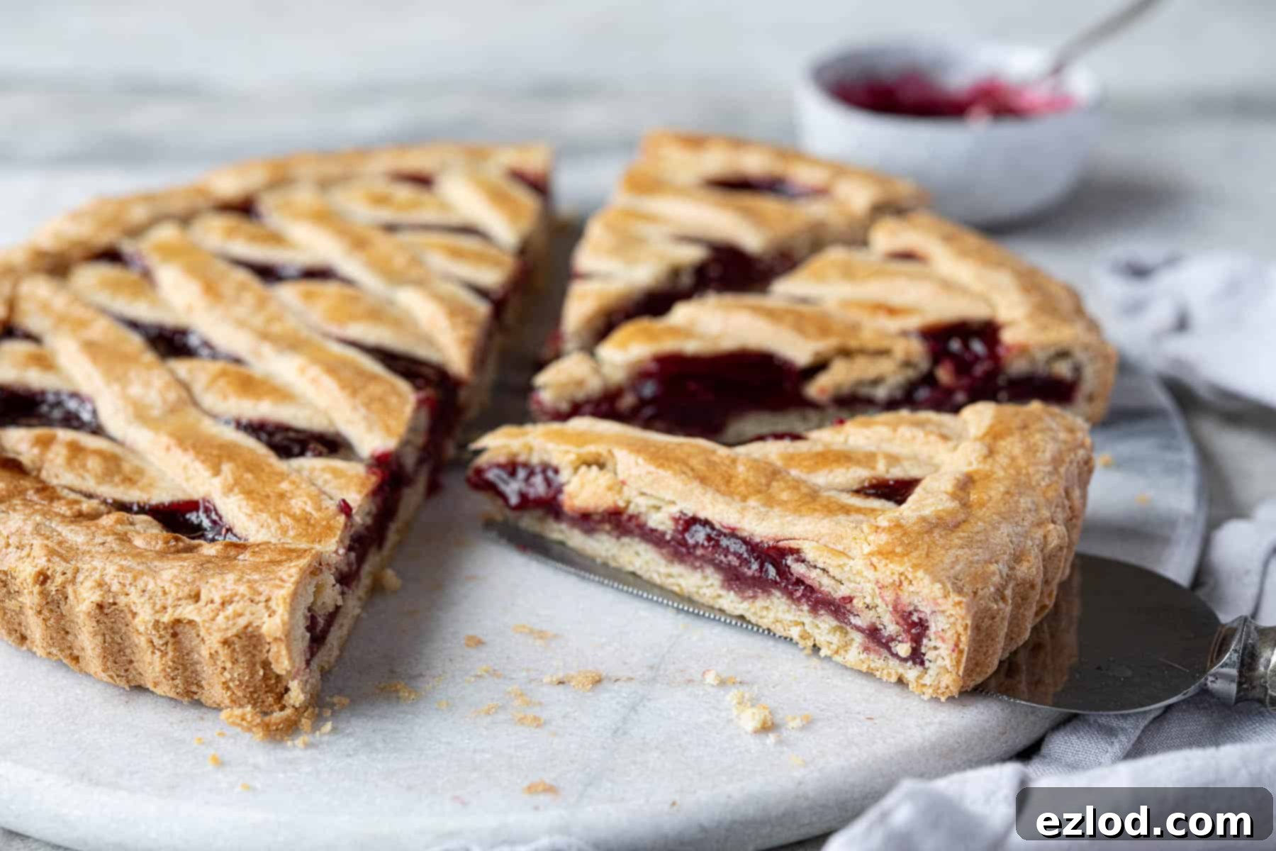 A close-up of a single slice of vegan jam crostata, presented beautifully on a plate, showing the layered golden pastry crust, the glistening fruit jam filling, and the tender, crumbly texture of the tart.