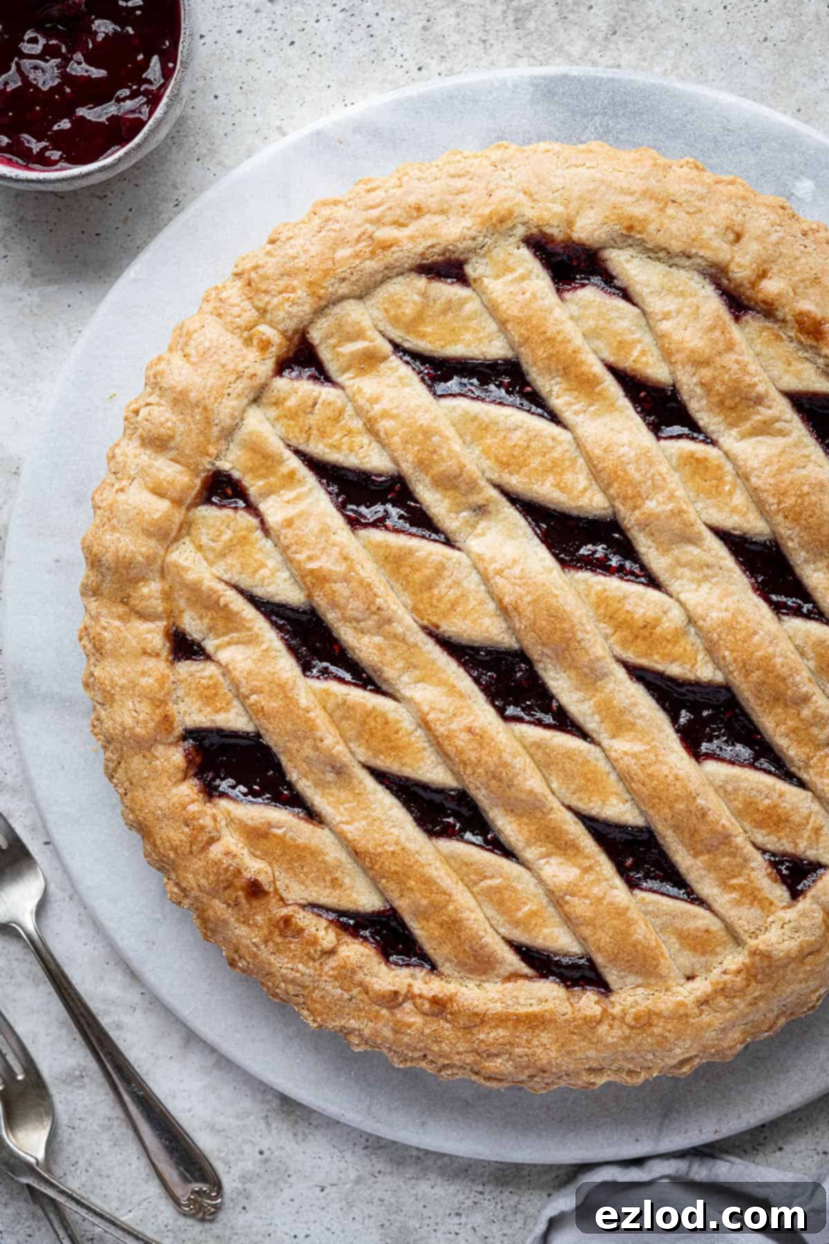 Close-up of a rustic vegan jam crostata with a perfect golden-brown lattice top, showcasing the visible fruit jam filling beneath. The pastry has a lovely crumbly texture and inviting sheen.