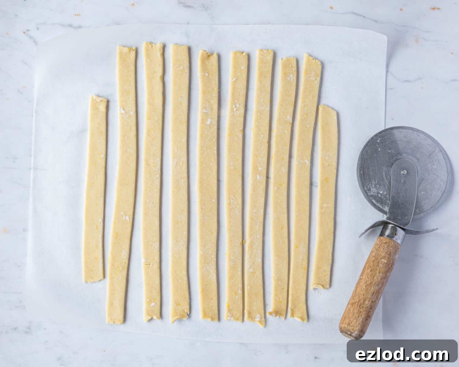 Precisely cut vegan pastry dough strips, arranged neatly on a floured surface, prepared for creating the traditional lattice top of the crostata.