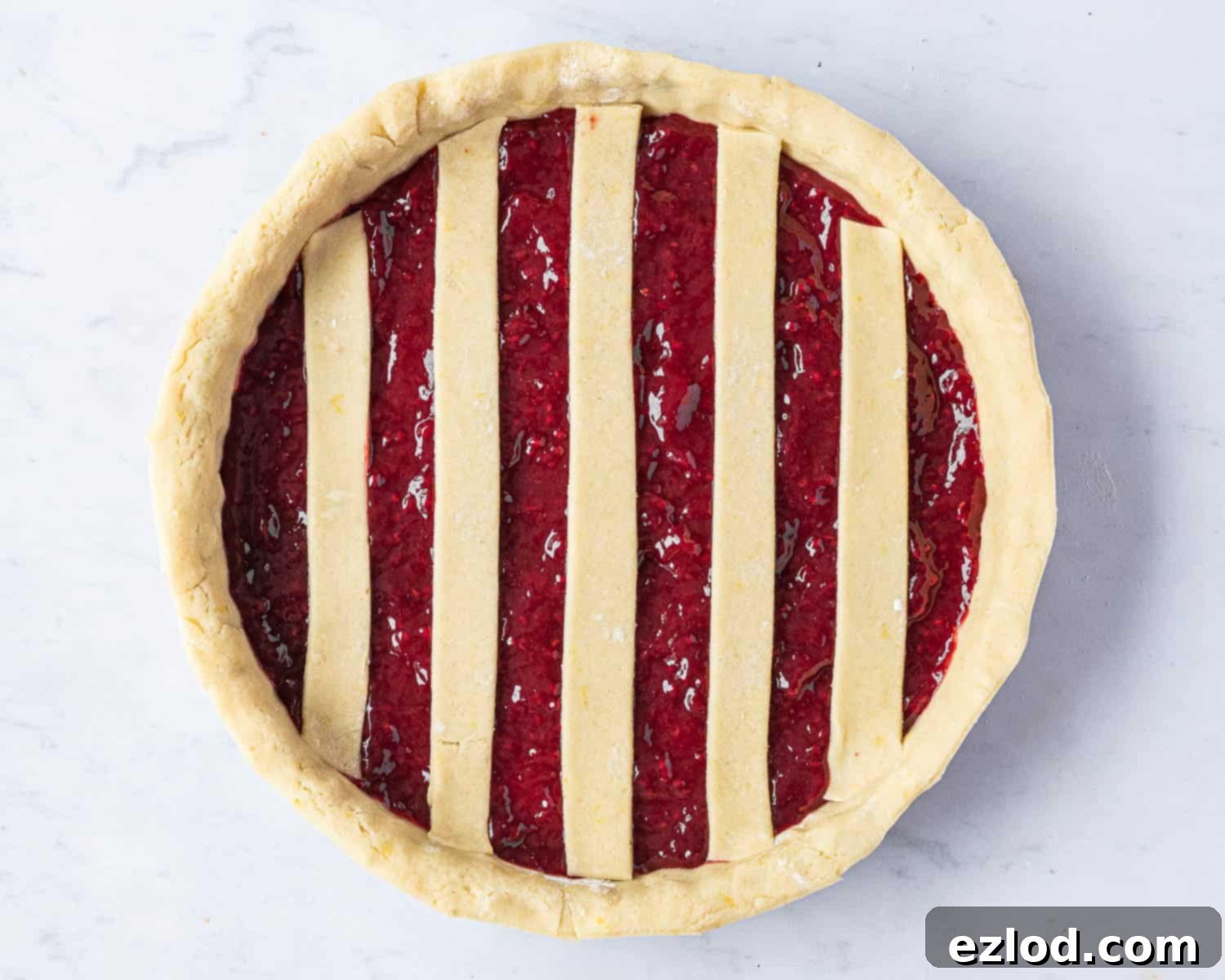 The jam-filled vegan crostata base with five pastry strips laid out horizontally and spaced apart, marking the initial step of the lattice pattern.
