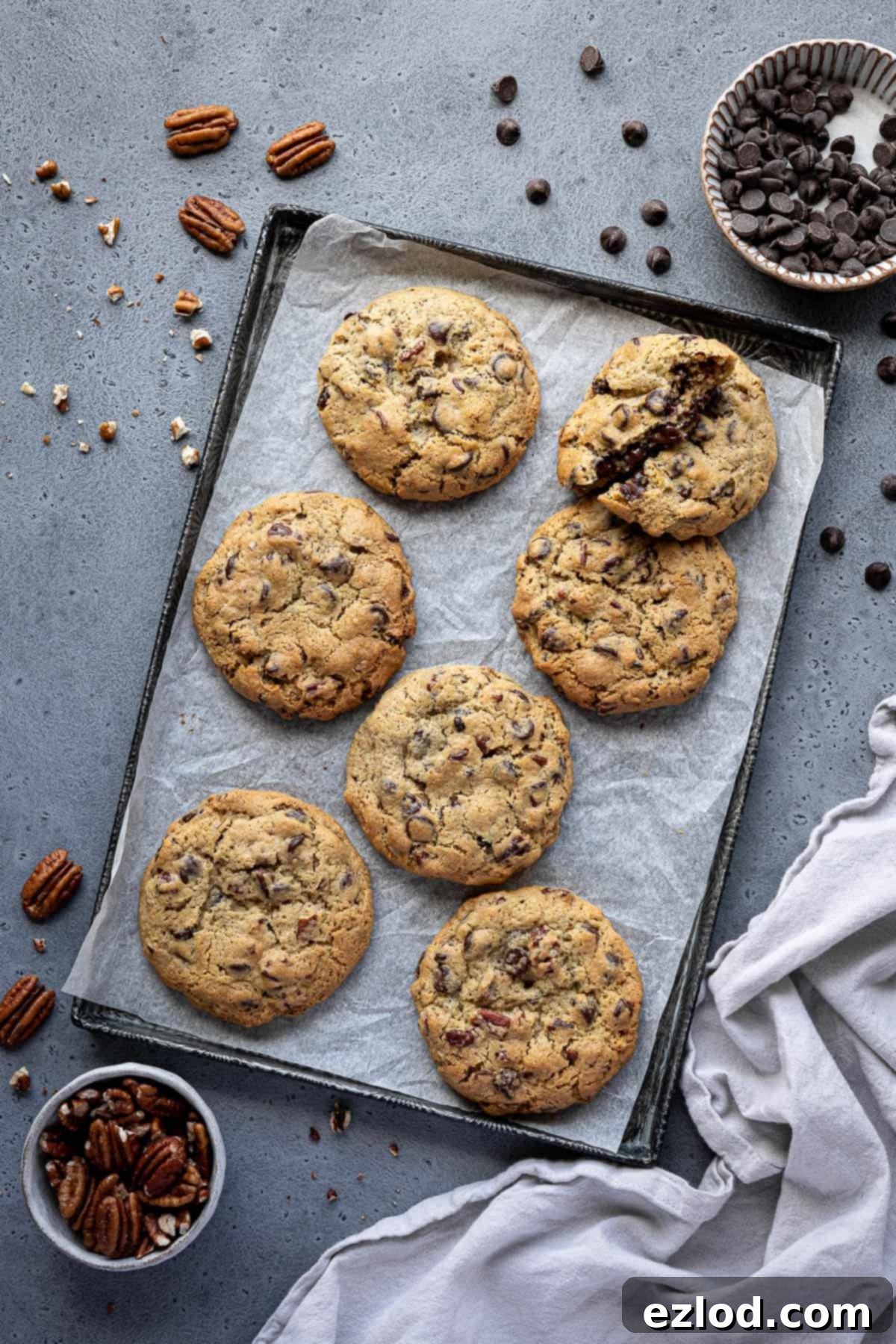 A tray of chunky chocolate pecan cookies, with separate bowls of chocolate chips and pecans.