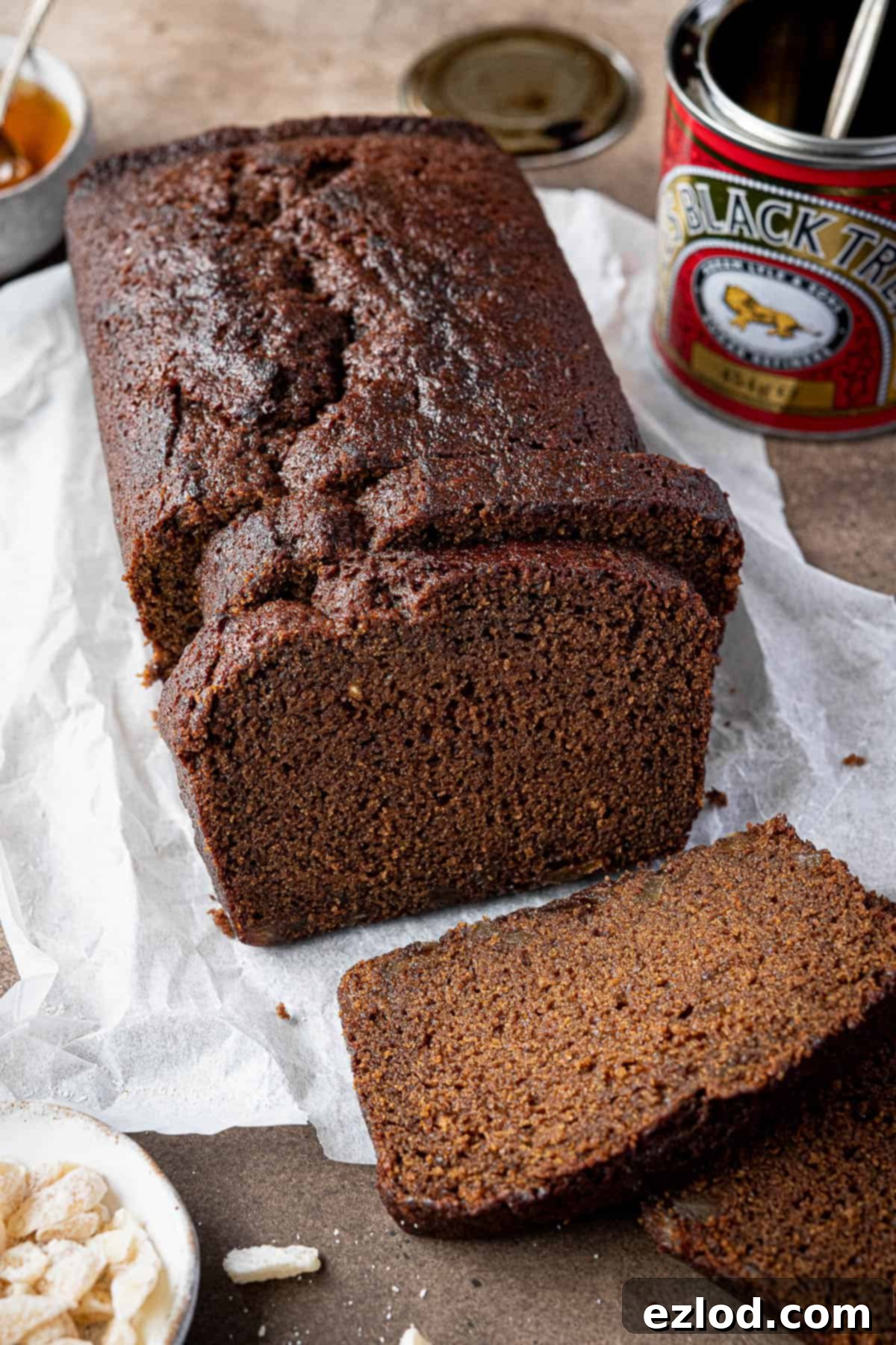 Vegan ginger loaf cake on a sheet of baking parchment with a tin of treacle.