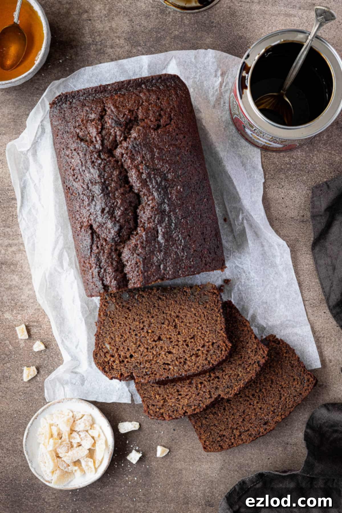 Vegan ginger loaf cake on a brown background with a tin of treacle and bowls of candied ginger and golden syrup.
