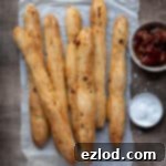 Artisan Sun Dried Tomato Breadsticks 10 Vegan sun dried tomato breadsticks on a sheet of baking parchment with bowls of sun dried tomatoes and salt.