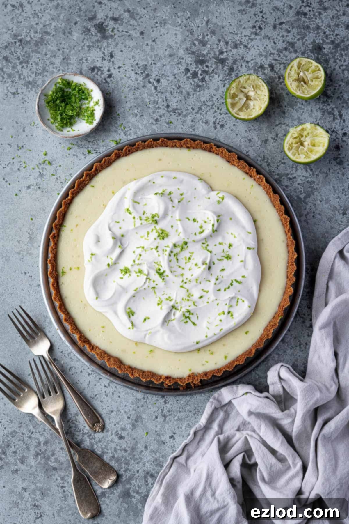 Tangy Vegan Key Lime Pie 2 Vegan key lime pie on a grey surface wiith lime halves, a bowl of lime zest and a pile of forks.
