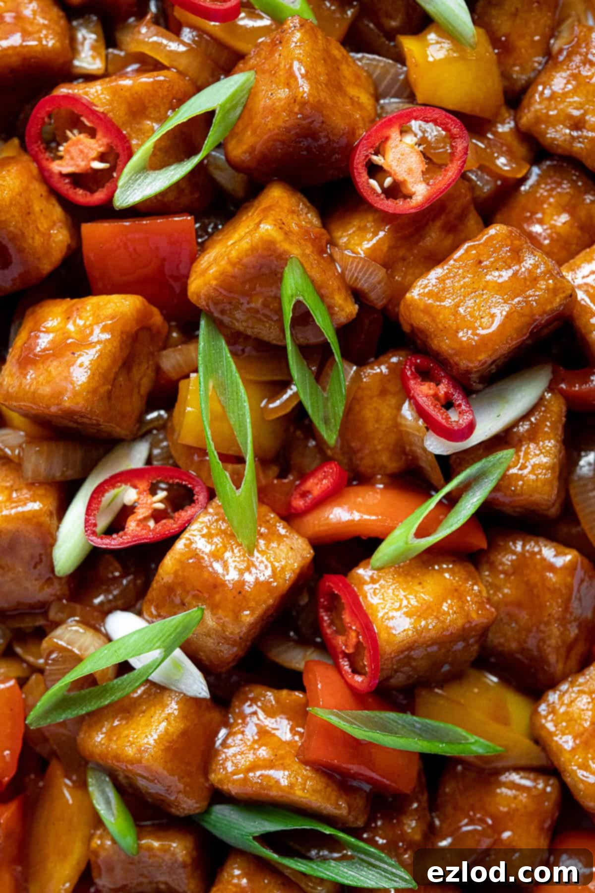 A close-up shot of crispy sweet and sour tofu cubes mixed with colorful bell peppers and sliced onions, glistening with the sticky pineapple sauce.