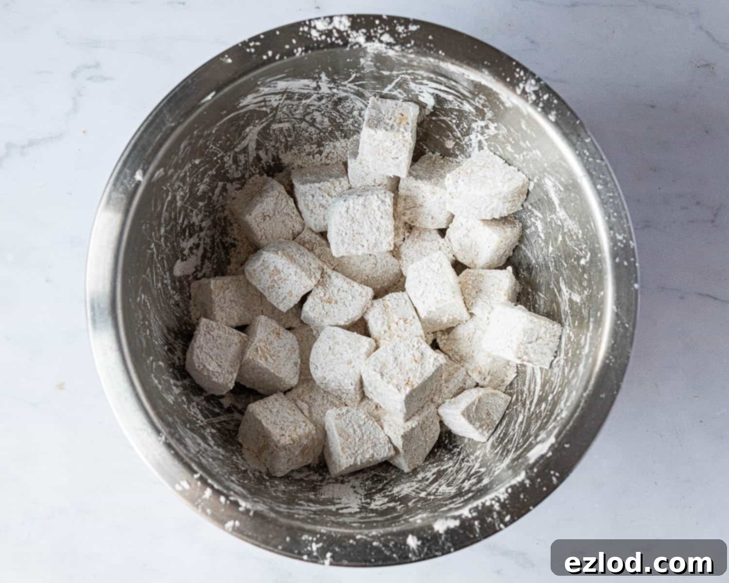 Step 2: Tofu cubes perfectly coated in a seasoned cornflour mixture, ready for frying to achieve maximum crispiness.