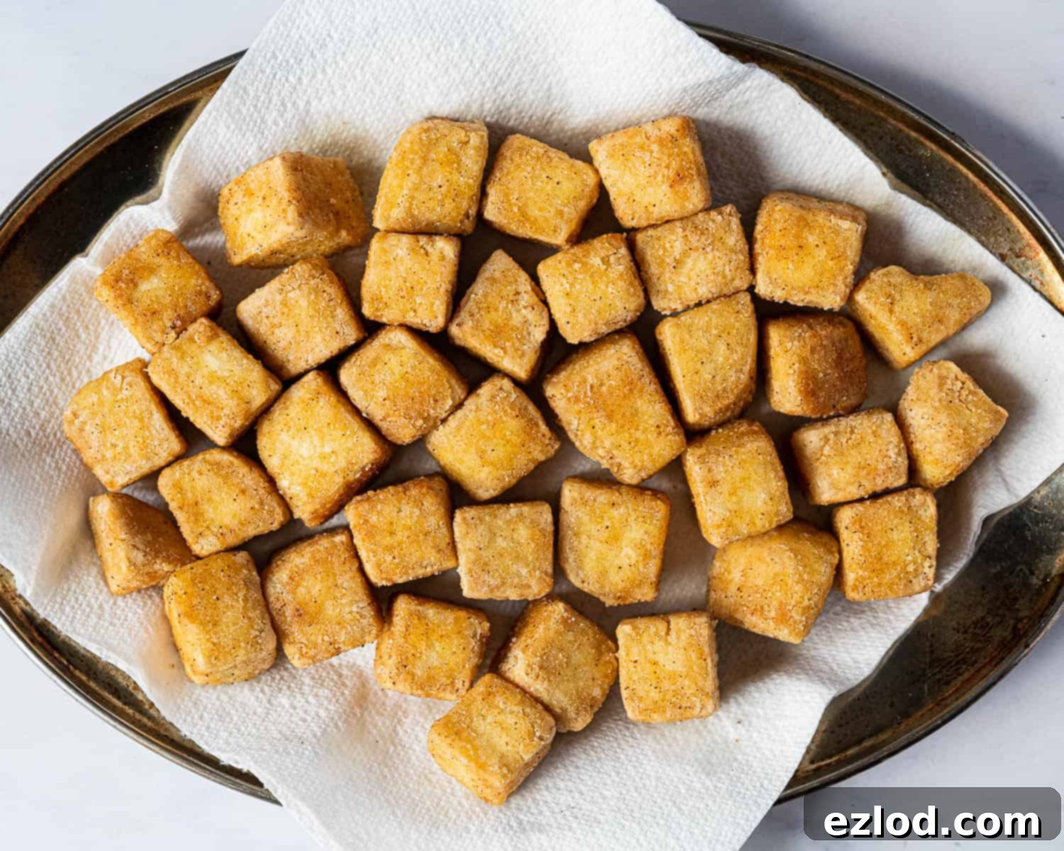 Step 3: Freshly fried, golden-brown tofu pieces resting on a paper towel-lined plate, draining excess oil and ready for the sauce.