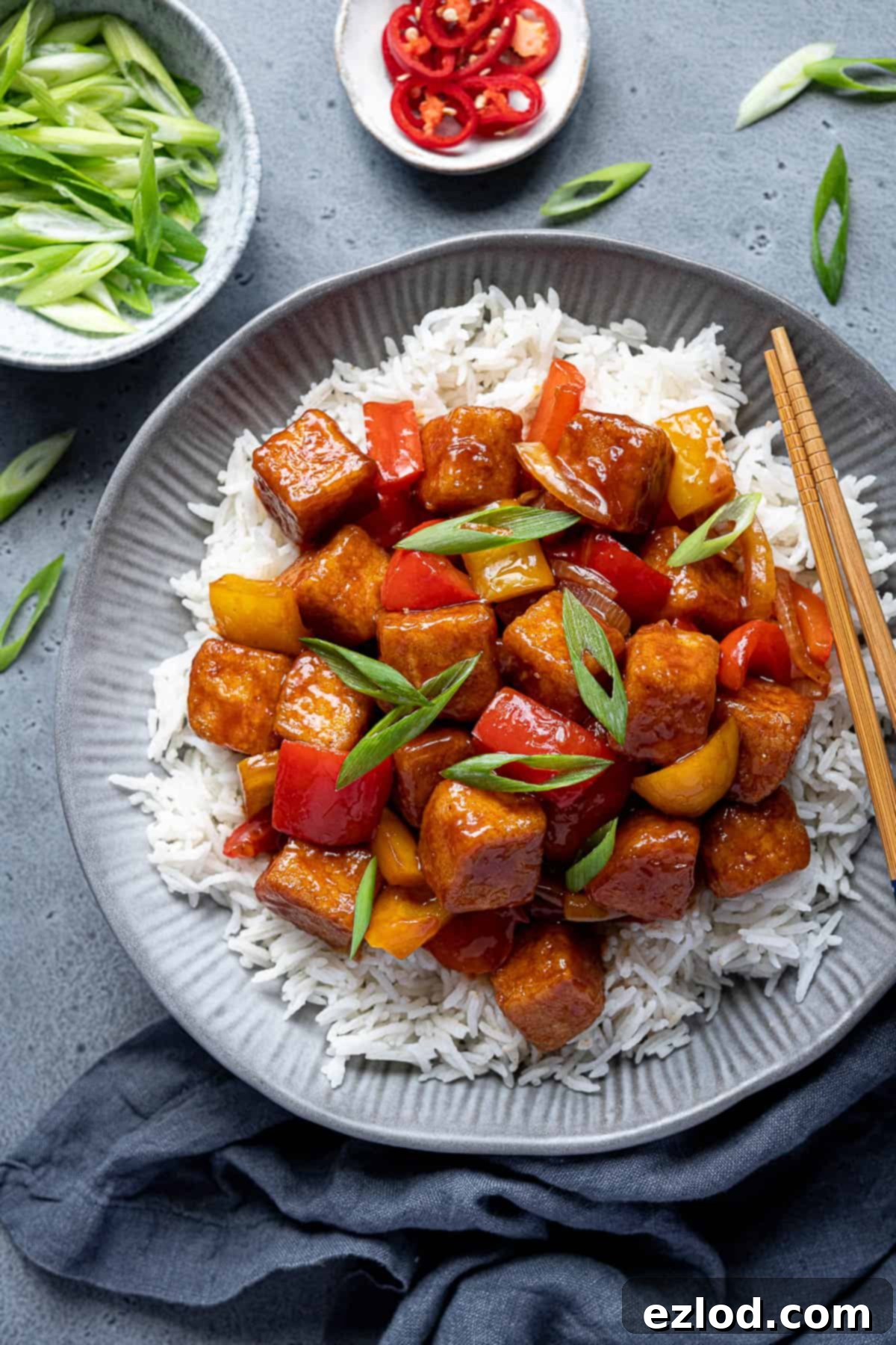 Sweet and sour tofu generously placed on a bed of white rice in a stylish grey bowl, ready to be enjoyed.