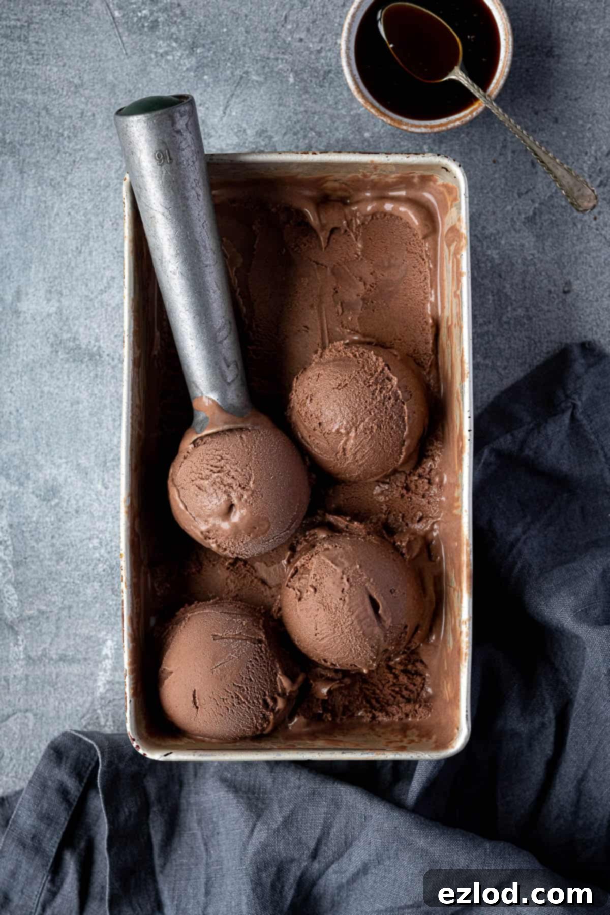 Veggan malted chocolate ice cream in a loaf tin with a bowl of malt extract, showcasing its rich, creamy texture.