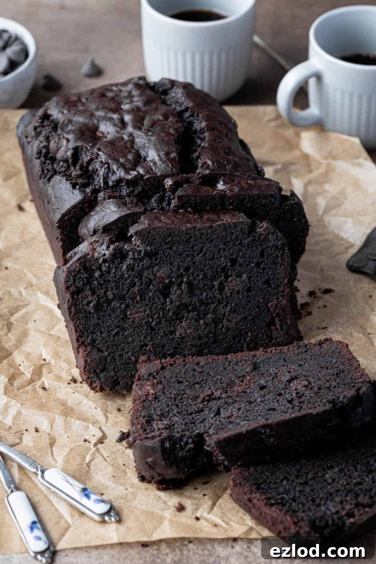 Vegan chocolate courgette cake with cups of coffee and a bowl of chocolate chips.