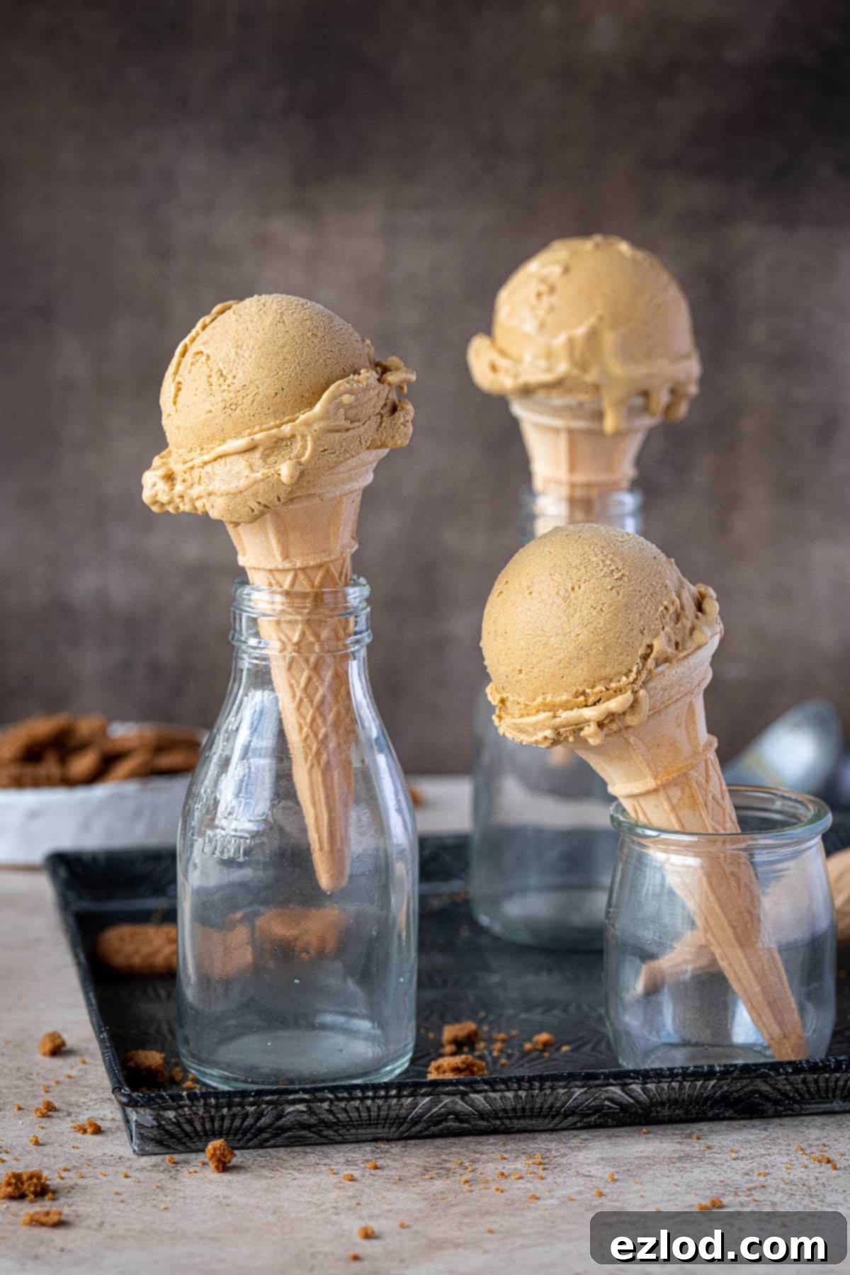 Three cones of vegan pumpkin ice cream in glass milk bottles with a bowl of crushed cookies.