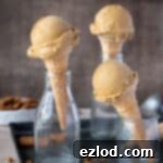 Three cones of vegan pumpkin ice cream in glass milk bottles with a bowl of crushed cookies.