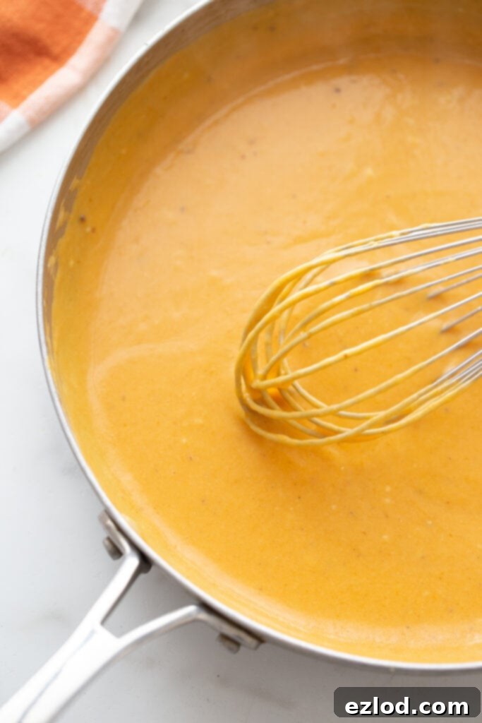Pumpkin puree being stirred into the creamy cheese sauce.