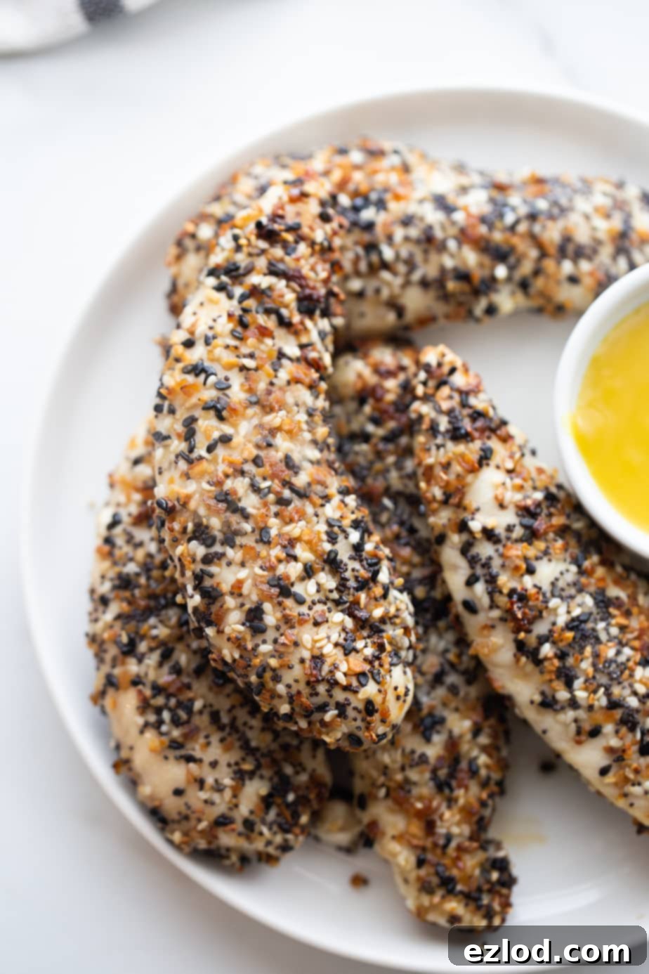 A close up of chicken tenders covered in everything bagel seasoning and maple mustard sauce on the side.