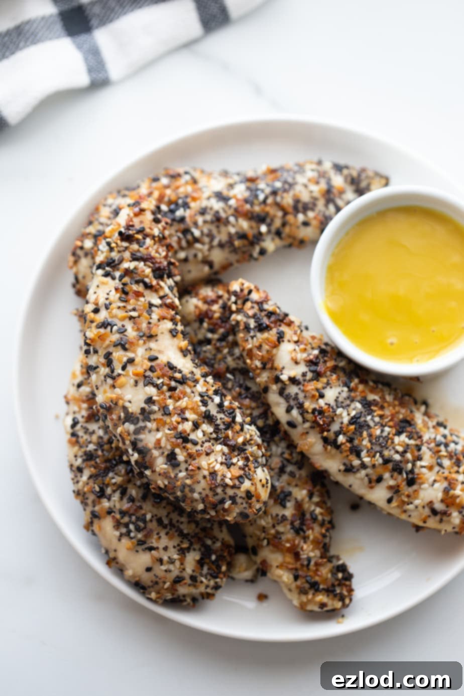 An overhead shot of chicken tenders covered in everything bagel seasoning and a white ramekin with maple mustard sauce.