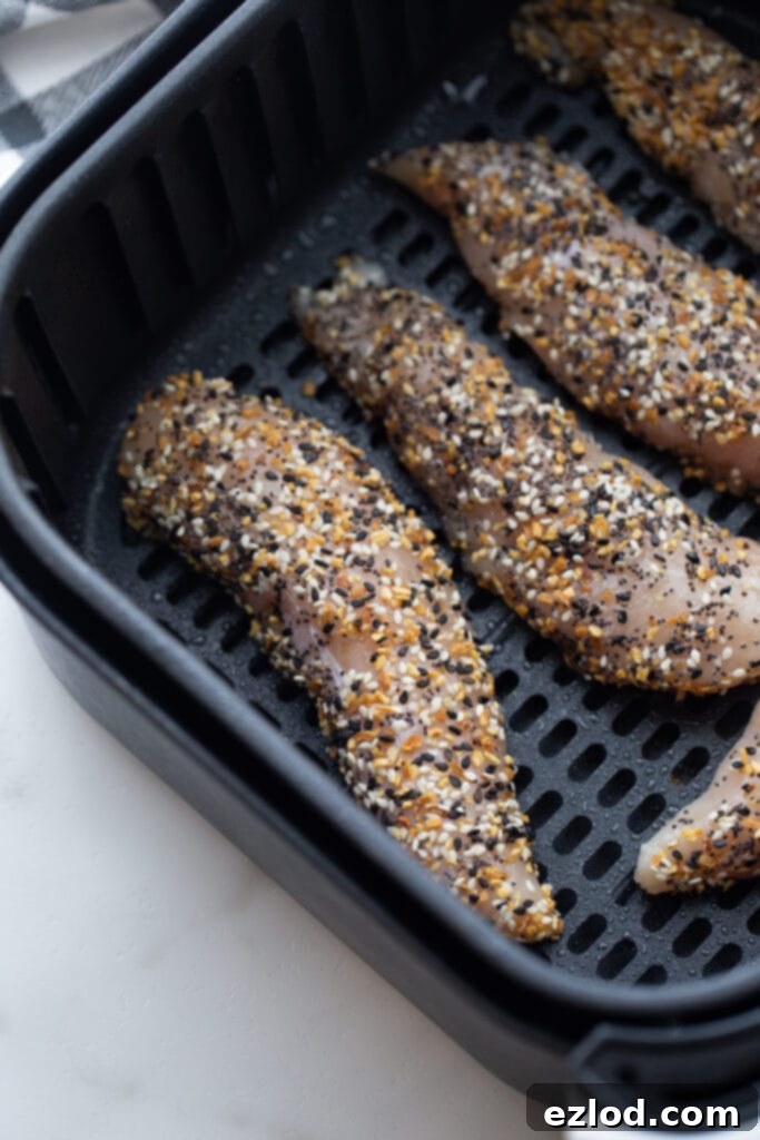 An overhead shot of an air fryer basket with raw chicken tenders covered in everything bagel seasoning.