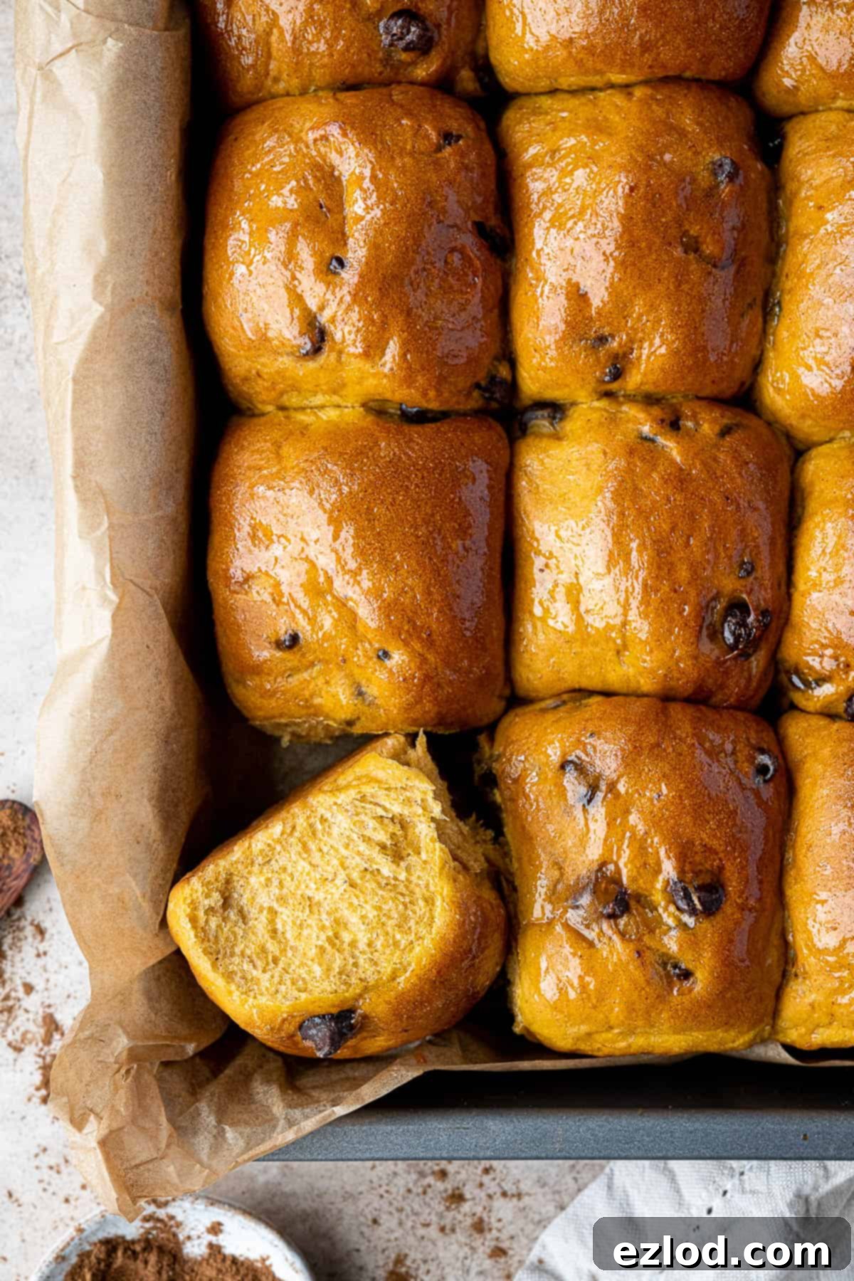 A close-up of baked pumpkin rolls in a tin, with one roll turned on its side to show its fluffy interior.