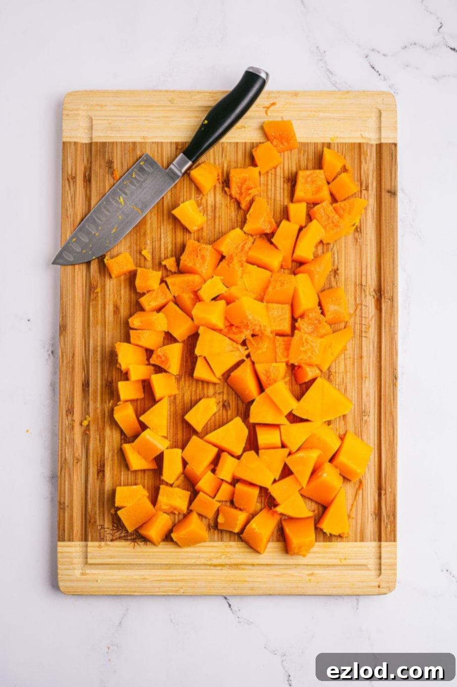 Overhead photo of cubed and cut butternut squash on a wooden cutting board with a chef's knife off to the side, showcasing the easy-to-manage pieces.